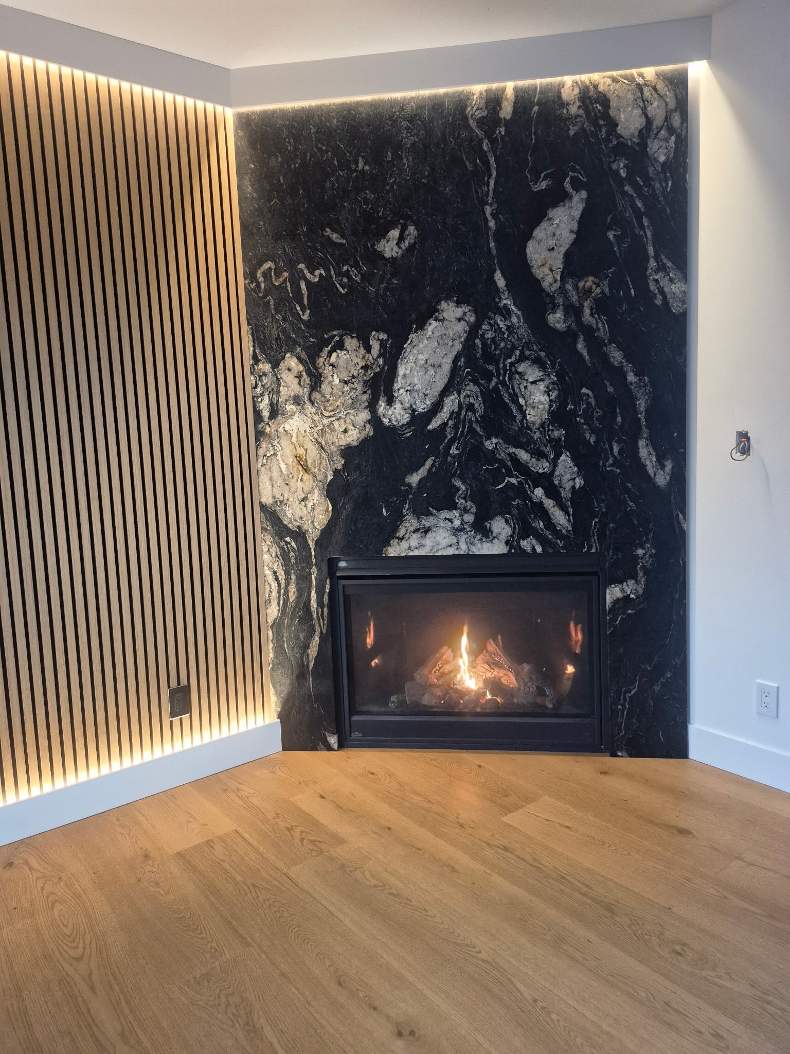 Corner gas fireplace with granite surround and lit wood slat wall installed by Central Air Solutions